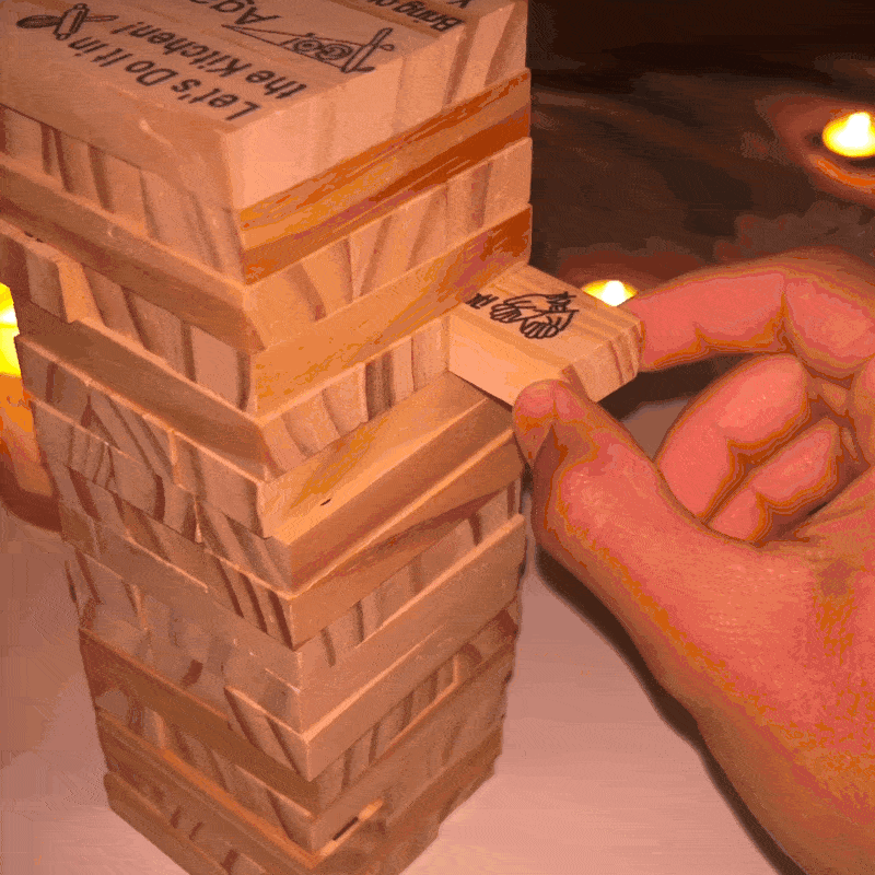 Hands carefully pulling a branded block from a candle-lit Jenga tower.